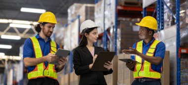 Depo çalışanları ve kadın denetçi envanter yönetimini tartışmak için dijital tablet ve pano kullanıyor. Modern lojistik ve tedarik zinciri operasyonlarında takım işbirliği kavramı.