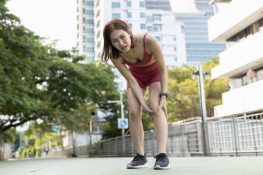 Aktif giysili Asyalı bir kadın, şehir merkezindeki idmandan sonra bacağındaki ağrıyla boğuşuyor. Spor sakatlığı, kas gerginliği, fitness meydan okuma ve fiziksel eğitimde farkındalık kavramı.