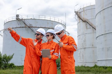 Turuncu güvenlik üniforması ve kasklı mühendisler bir petrol rafinerisinde birlikte çalışıyorlar, takım çalışması, iletişim ve enerji endüstrisinde liderlik ile operasyonlar planlıyorlar..