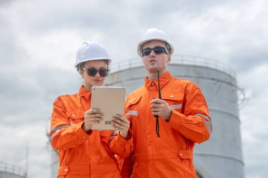 Petrol rafinerisinde tablet ve telsiz kullanan turuncu üniformalı mühendisler enerji endüstrisinde iletişim, planlama ve takım çalışması sergilediler..