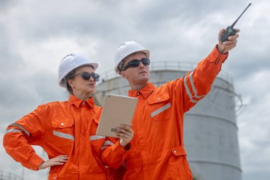 Petrol rafinerisinde tablet ve telsiz kullanan turuncu üniformalı mühendisler enerji endüstrisinde iletişim, planlama ve takım çalışması sergilediler..