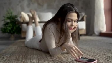 Yakın plan esmer blogcu yerde yatıp telefona bakıyor.