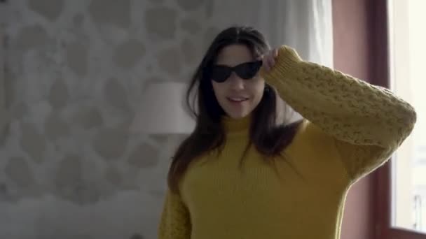 Крупним планом дівчина розважається вдома в стильних окулярах в жовтому светрі — стокове відео