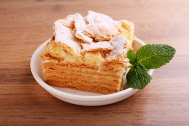 Napolyon pastası, vanilyalı süt kreması ile süslenmiş, naneli, ahşap bir arka planda bir tabakta.