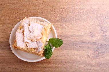 Napolyon pastası, vanilyalı süt kreması ile süslenmiş, naneli, ahşap bir arka planda bir tabakta.