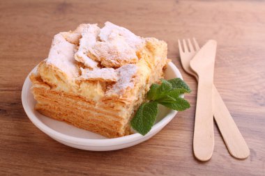 Napolyon pastası, vanilyalı süt kreması ile süslenmiş, naneli, ahşap bir arka planda bir tabakta.