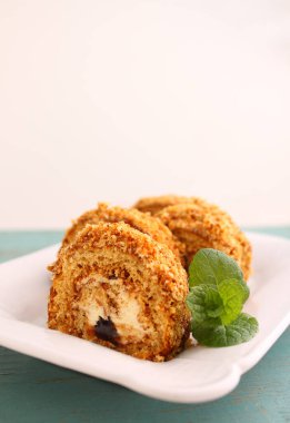 Tereyağlı kremalı kek ruloları hafif arka planda bir tabakta naneyle süslenmiş, seçici odaklı..