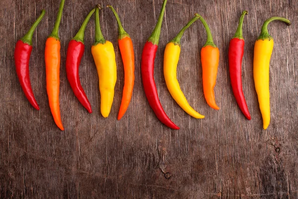 Hot red, yellow, orange peppers on the old wooden background — Stock Photo, Image