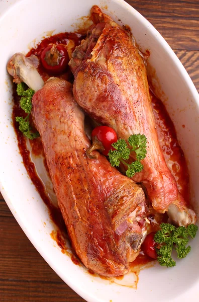 Baked turkey legs in white plate on dark background