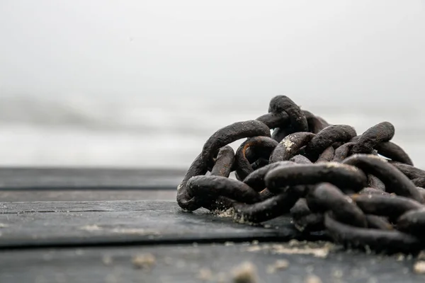 Closeup of rusty chain on a beach on wooden bridge
