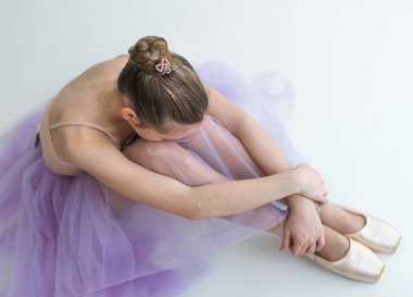 Genç kız yerde oturuyor, beyaz arka planda sivri uçlu ayakkabılar giyiyor. Genç ressam kavramı.