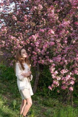 Çiçek ağacının yanında pembe çiçeklerle poz veren güzel bir kızın portresi. Kavram - bahar, çiçek, bahçede bir yürüyüş.