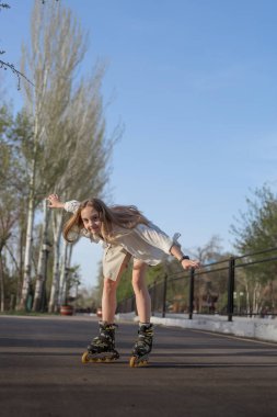 Genç bir kız güneşli bir günde parkta paten kayıyor. Kavram, çocuklara boş zamanlarında yararlı aktiviteler sunmaktır..