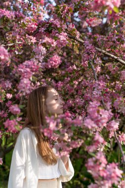 Çiçek ağacının yanında pembe çiçeklerle poz veren güzel bir kızın portresi. Kavram - bahar, çiçek, bahçede bir yürüyüş.