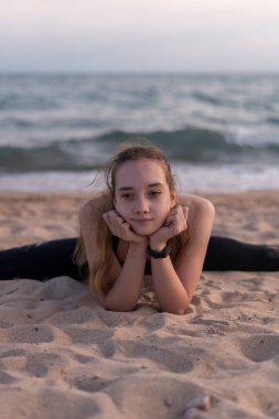 Gün batımında sahilde jimnastik, yoga, meditasyon ve ayrılık eğitimi alan genç bir kız. Konsept - gençler için egzersiz ve sağlık hizmetleri hakkında.