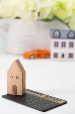 Küçük bir oyuncak ev, bir arabanın arka planına karşı bir hesap makinesinin üzerinde durur. Doğru bir finansal hesaplama başarının anahtarıdır.