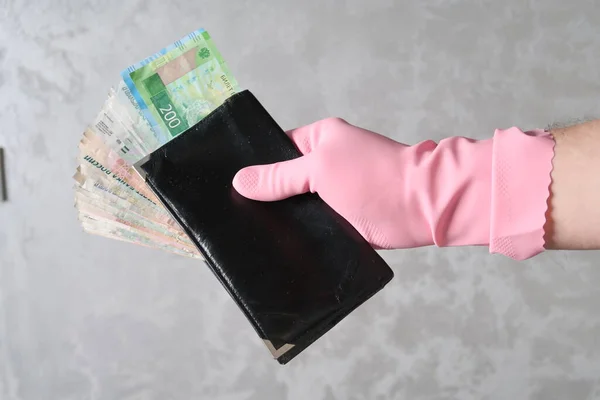 A hand in a glove holds a wallet with a bundle of Russian banknotes