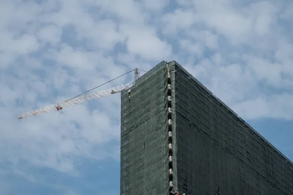 İnşaat halindeki yüksek bina tamamen yeşil inşaat ağı, inşaat vinci ile kaplı.