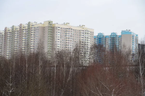 Massive residential buildings on the edge of a deep cliff overgrown with trees, snow, winter, background