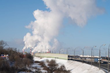 Soğuk ve güneşli bir günde büyük bir ısıtma istasyonunun dumanının arka planına karşı otoyol.
