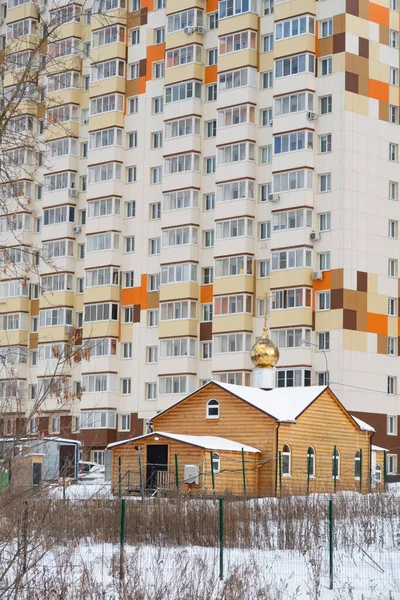 A small new log church against the background of a high residential building, Moscow region