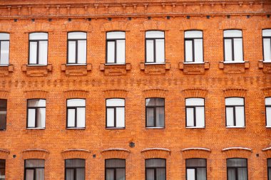 Çok sayıda kemerli penceresi ve arka planı olan eski kırmızı tuğladan bir binanın ön cephesi