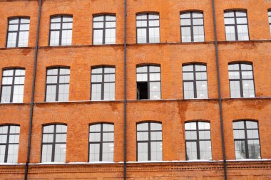 Kırmızı tuğlalı bir binanın ön cephesinde birçok kavisli pencere, bir pencere açık.