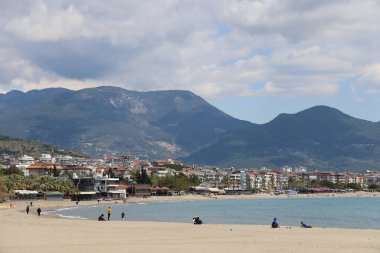 Deniz kıyısındaki tatilciler konut binalarının arka planına karşı, Alanya, Nisan 2021