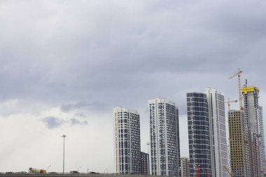 Bulutlu bir arka plan, inşaat vinçleri ve arka planda modern binaların inşası