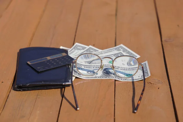 木製の板の上に眼鏡をかけた電卓や銀行券の財布 — ストック写真