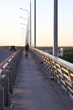 Bir bisikletçi ve bir araba Volga üzerinde bir köprü üzerinde, akşam, Dubna, Moskova bölgesi, Temmuz 2021