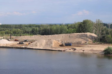 Nehir iskelesindeki kamyonlara toprak yüklemek, nehir kıyısındaki çakıl yığınları