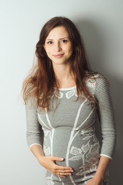 gri elbiseli duran sevimli hamile kadın