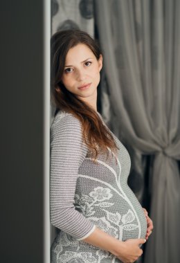 gri elbiseli duran zarif hamile kadın