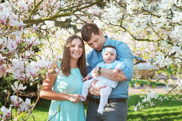 Familia feliz con linda hija bebé en los árboles de flores —  Fotos de Stock