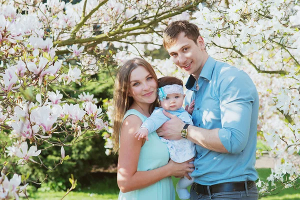 Familia feliz con linda hija bebé en los árboles de flores —  Fotos de Stock