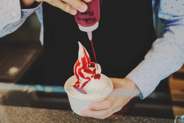 Verkäufer gießt Sauce auf einen weich gefrorenen Joghurt in wite Take-away-Tasse — Stockfoto