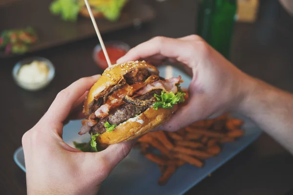 Człowiek posiada burger z rąk i słodkie ziemniaki frytki i spadki na — Zdjęcie stockowe