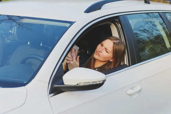 Jonge vrouw met behulp van mobiele telefoon tijdens het rijden van een auto — Stockfoto