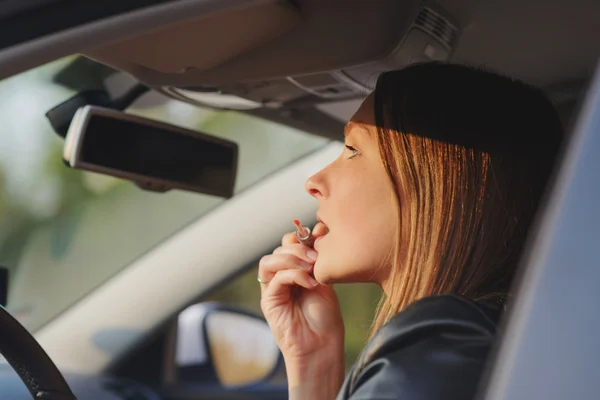 Jonge vrouw met behulp van lipgloss in auto — Stockfoto