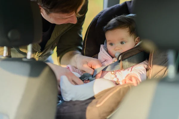 A father putting his baby daughter into her car seat in the car — Stock Photo, Image