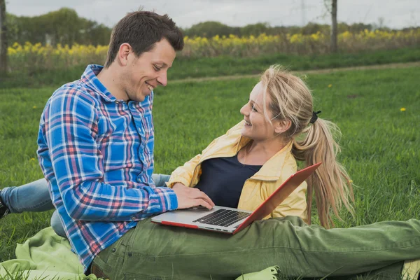 Schönes Paar liegt im Gras und arbeitet am Laptop — Stockfoto