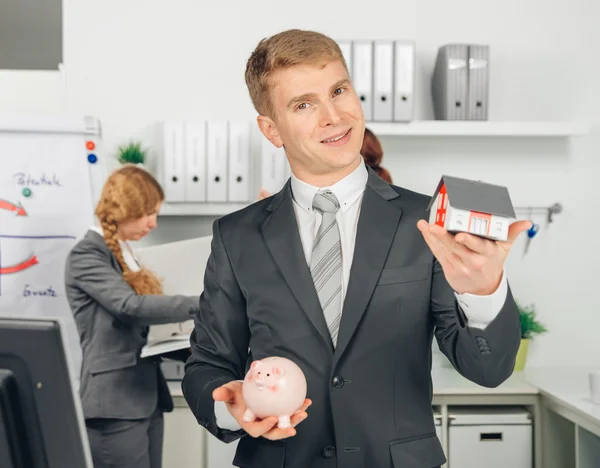 Handsome man holding house and piggybank — Stock Photo, Image