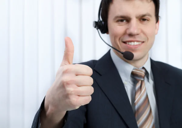 Business man in office speaks on headset shows thumb up — Stock Photo, Image