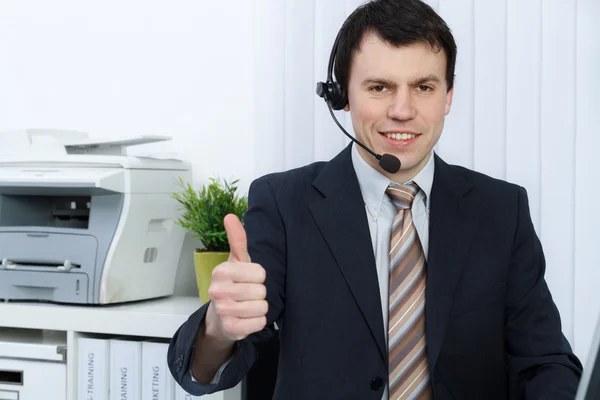 Business man in office speaks on headset shows thumb up — Stock Photo, Image