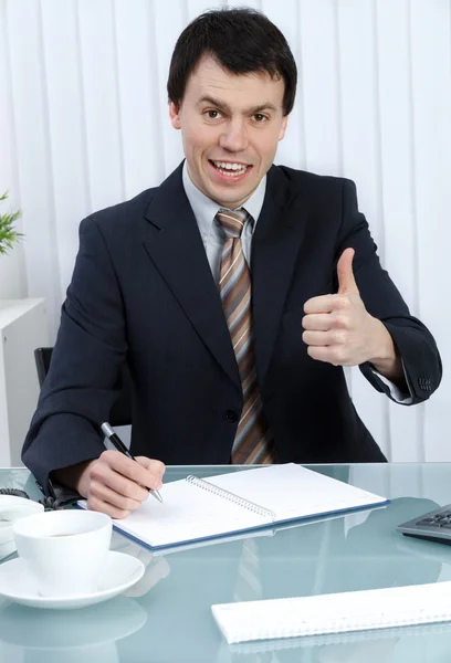 Бизнесмен в офисе, пишущий в дневном планировщике показывает большой палец вверх — стоковое фото