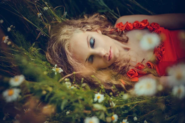 Mulher bonita em vestido vermelho deitado em flores — Fotografia de Stock