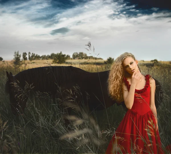 Hermosa mujer rubia en vestido rojo delante del caballo negro —  Fotos de Stock