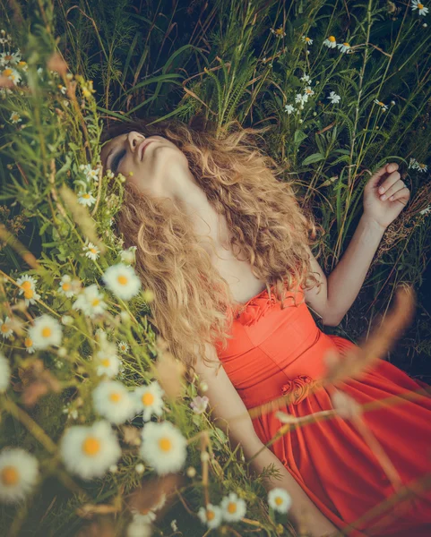 Mooie vrouw in rode jurk liggen in bloemen — Stockfoto