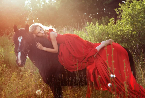 Piękne blond kobieta w czerwonej sukience na czarnego konia — Zdjęcie stockowe